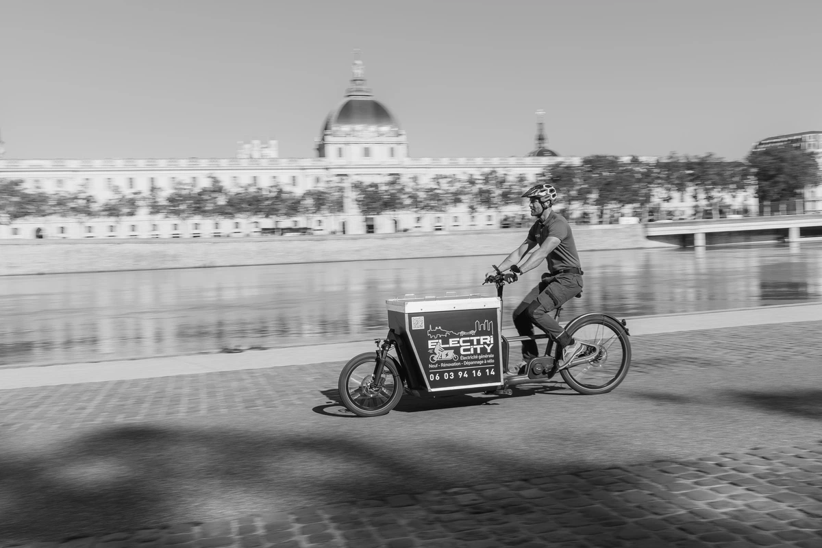 Technicien d'ElectriCity se déplaçant en vélo cargo pour installer une borne de recharge pour véhicules électriques en milieu urbain.